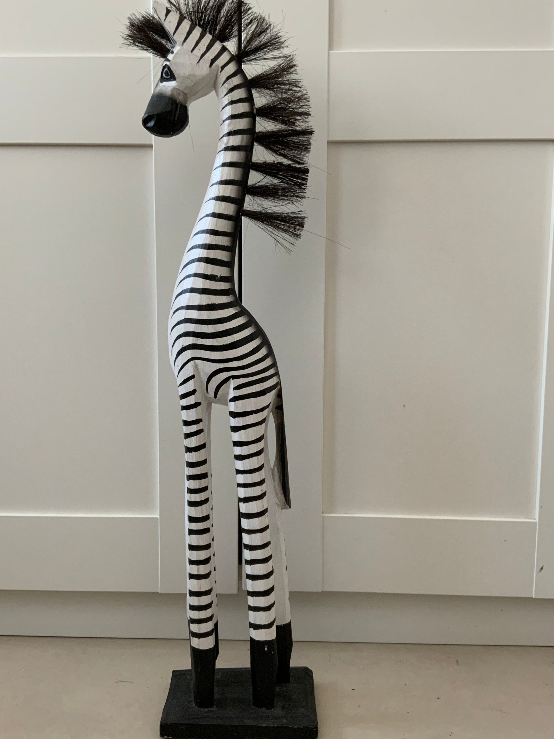 62 cm tall hand-carved wooden zebra figurine with black and white hand-painted stripes and a bristle mane, standing on a black wooden base against a white background.