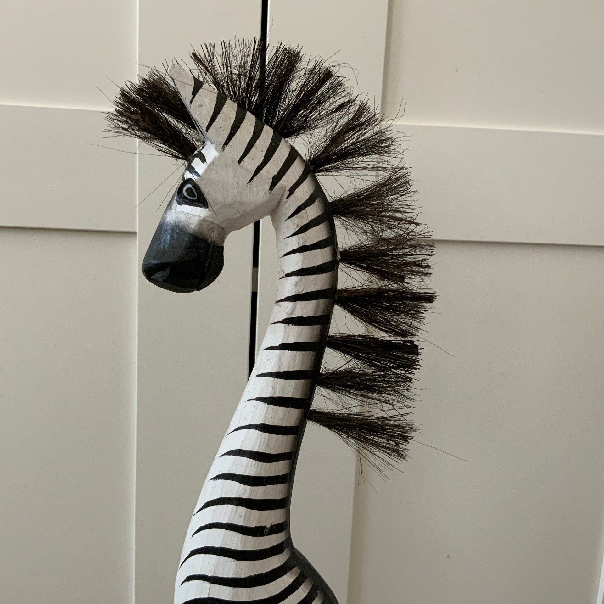 62 cm tall hand-carved wooden zebra figurine with black and white hand-painted stripes and a bristle mane, standing on a black wooden base against a white background.