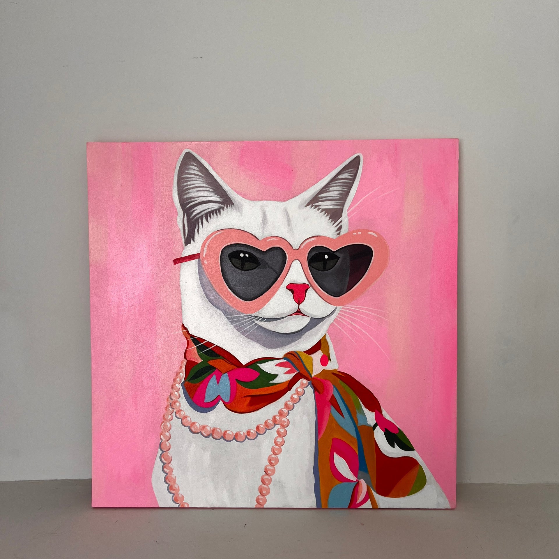 A vibrant pop-art style painting of a white cat wearing pink heart-shaped sunglasses, a multicolored floral silk scarf, and a string of pink pearls against a bright pink background.
