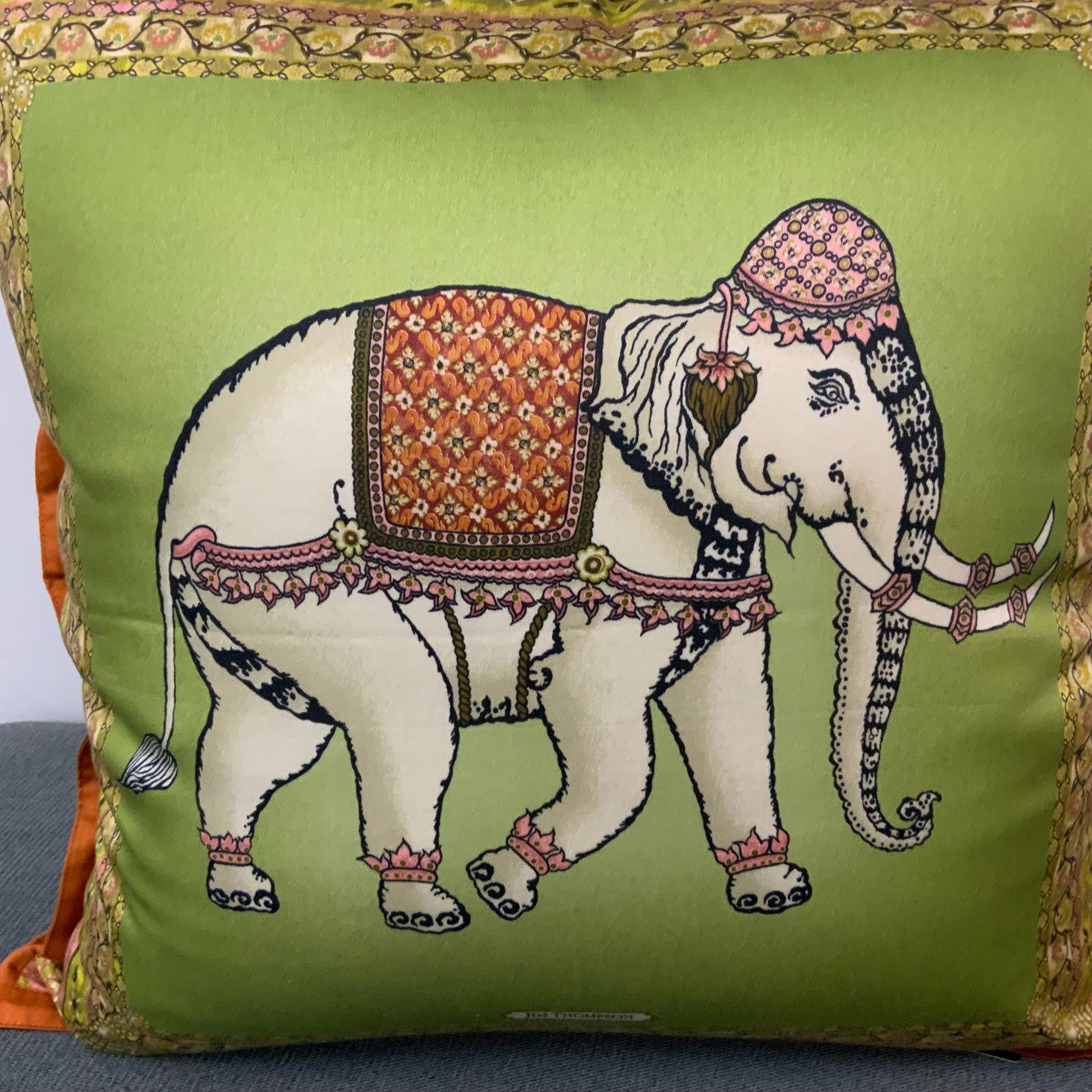 Jim Thompson luxury Thai silk decorative pillow featuring a white ceremonial elephant motif on a moss green background with a terracotta orange border.