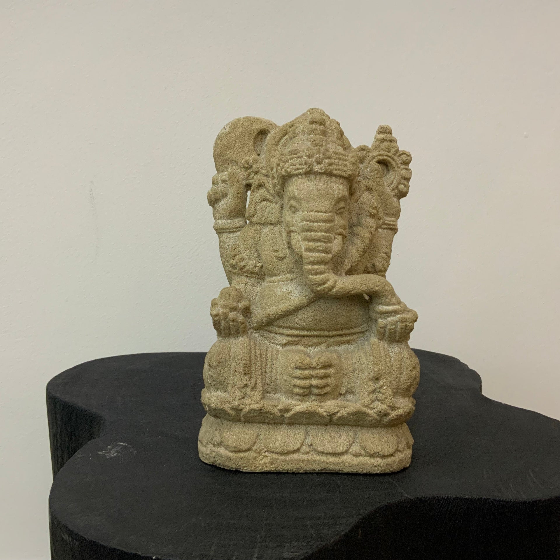 Ganesha Lord stone sculpture of a seated figure on a black pedestal against a white wall