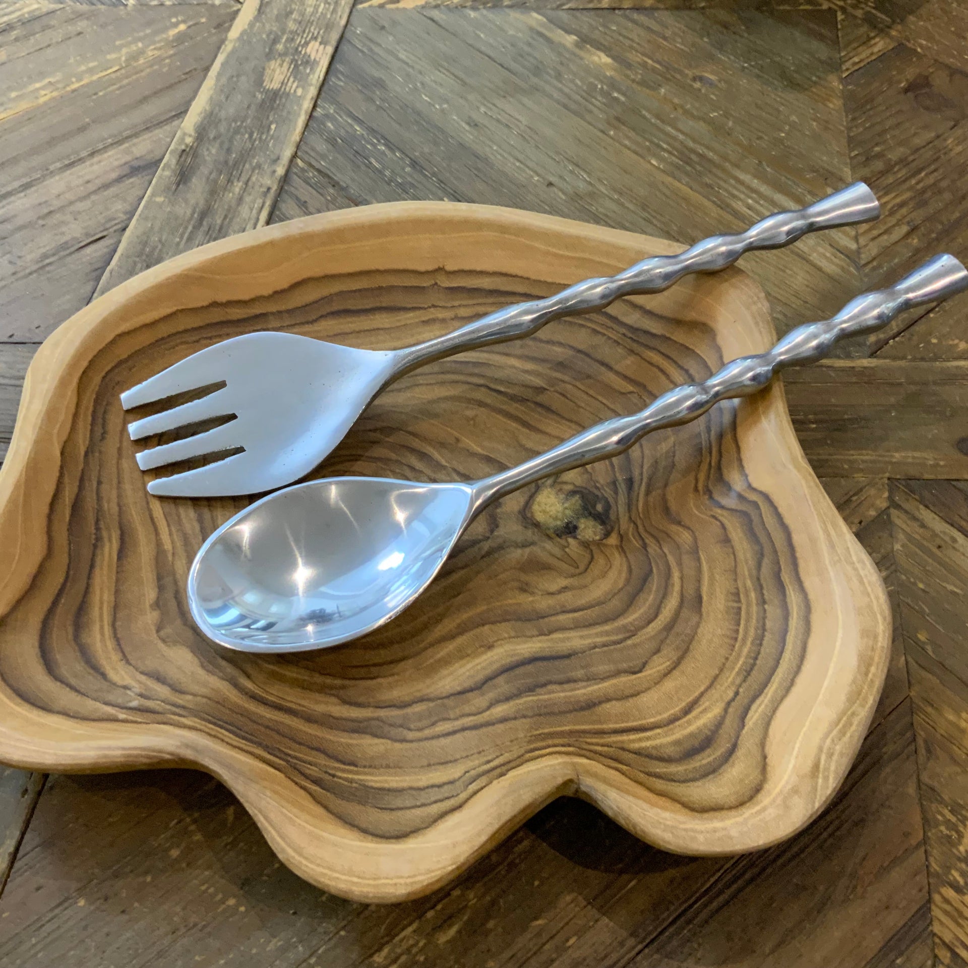 Hand fringe silver serving spoon and fork set resting in a wooden salad bowl.