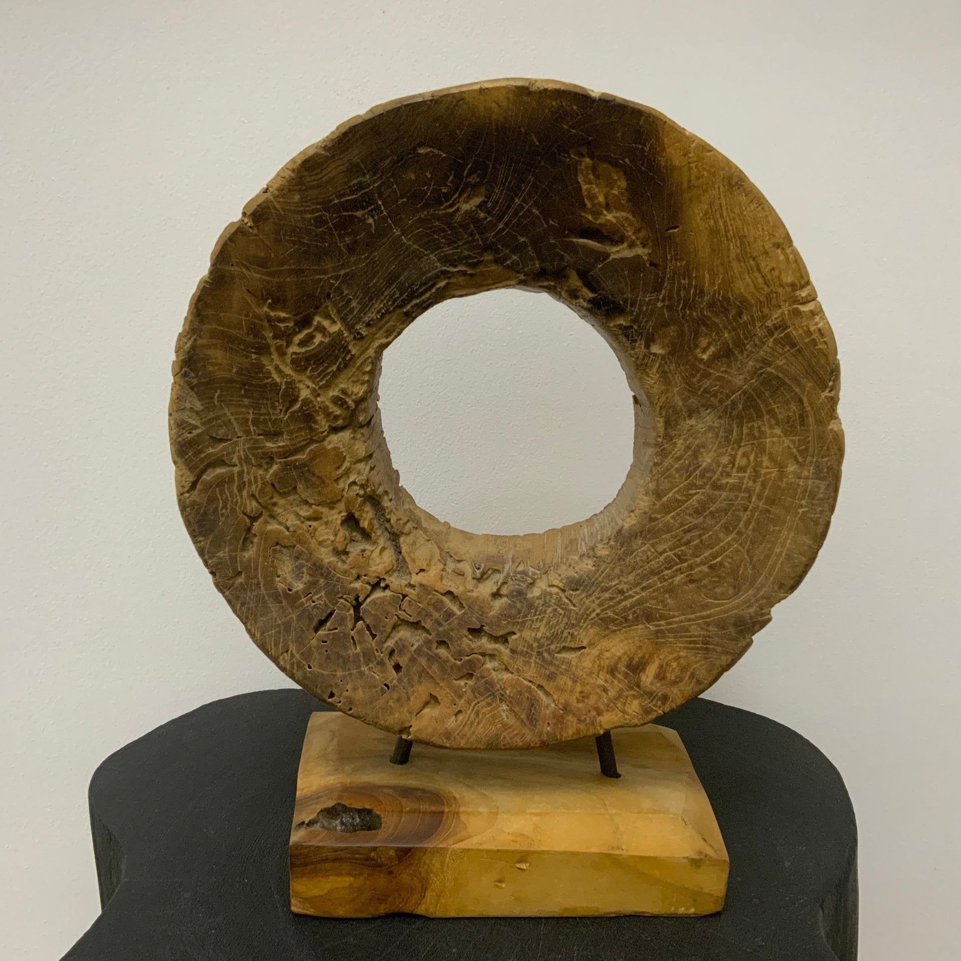 Hand-carved circular wood sculpture with natural grain and weathered textures, mounted on a solid wood base with thin metal rods.
