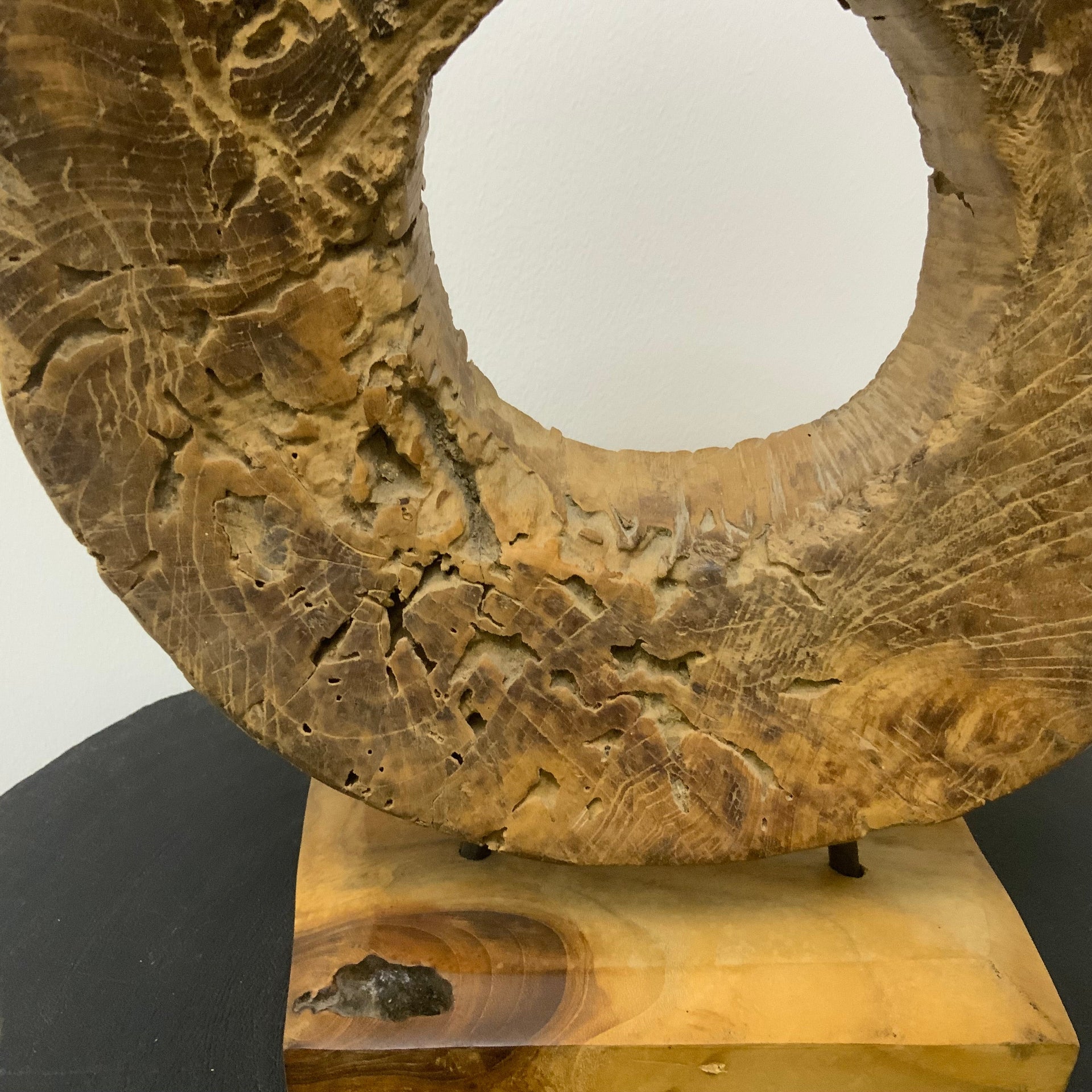 Hand-carved circular wood sculpture with natural grain and weathered textures, mounted on a solid wood base with thin metal rods.