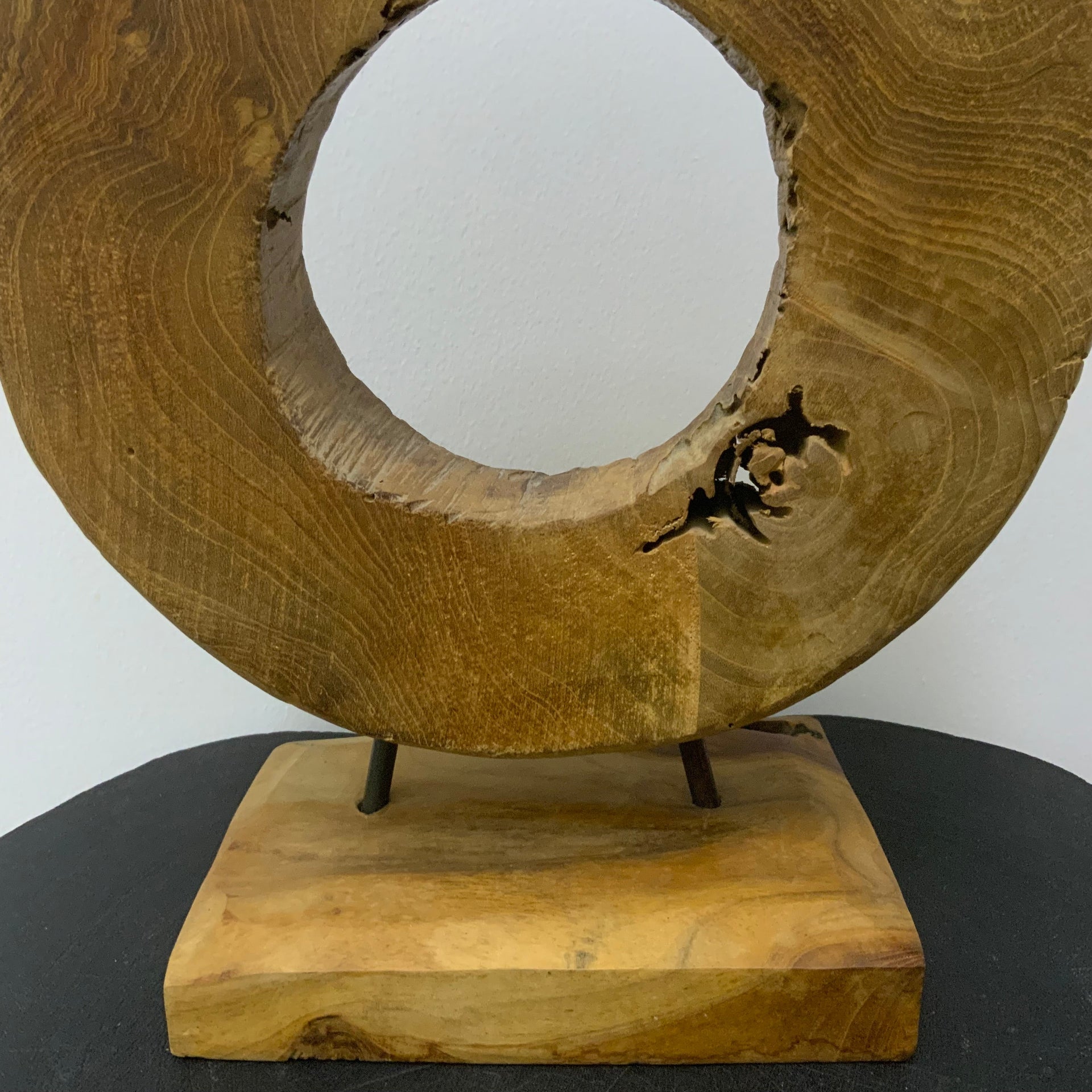 Hand-carved circular wood sculpture with natural grain and weathered textures, mounted on a solid wood base with thin metal rods.