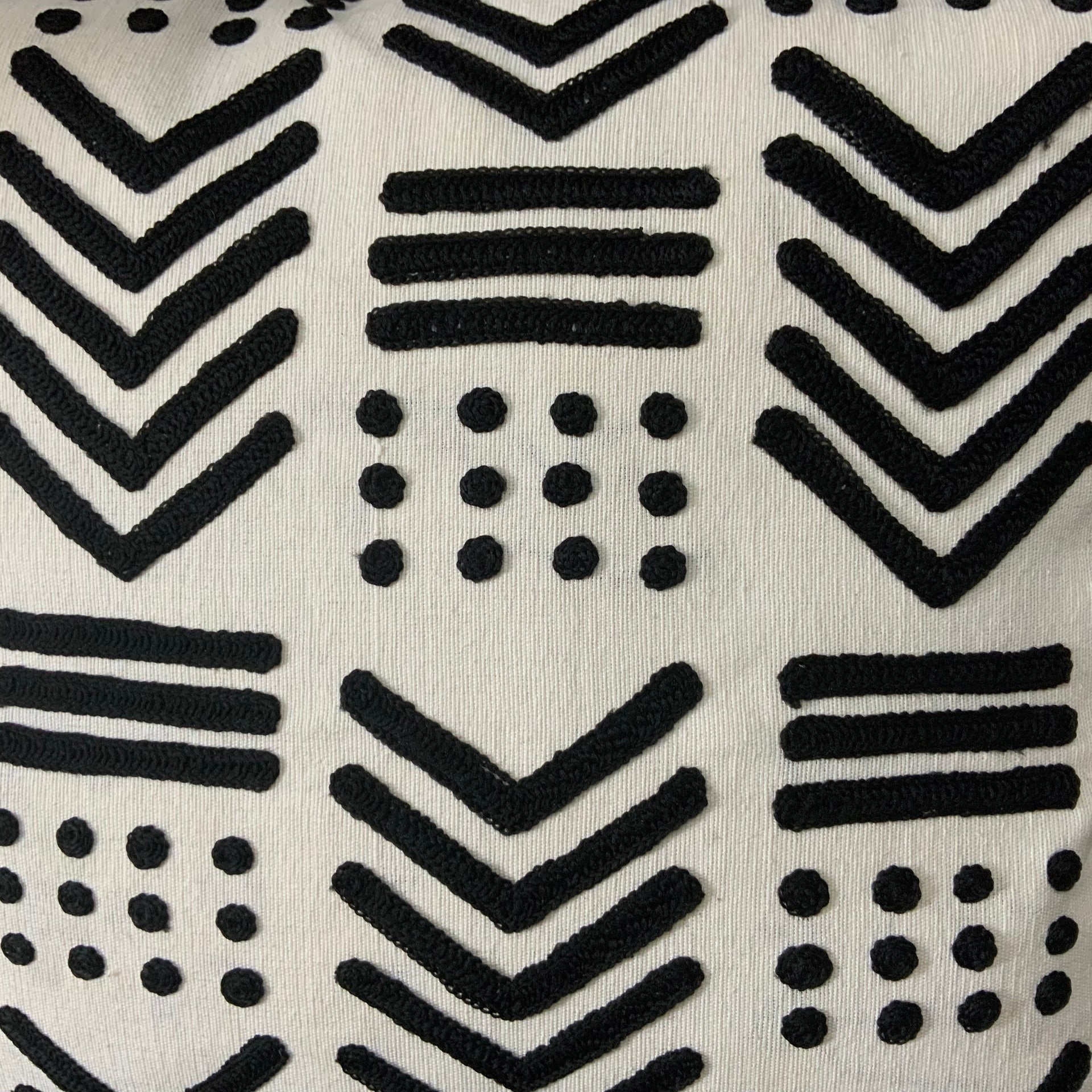 Square cream-colored throw pillow cover featuring raised black geometric embroidery in a tribal mudcloth pattern with chevrons, stripes, and dots.