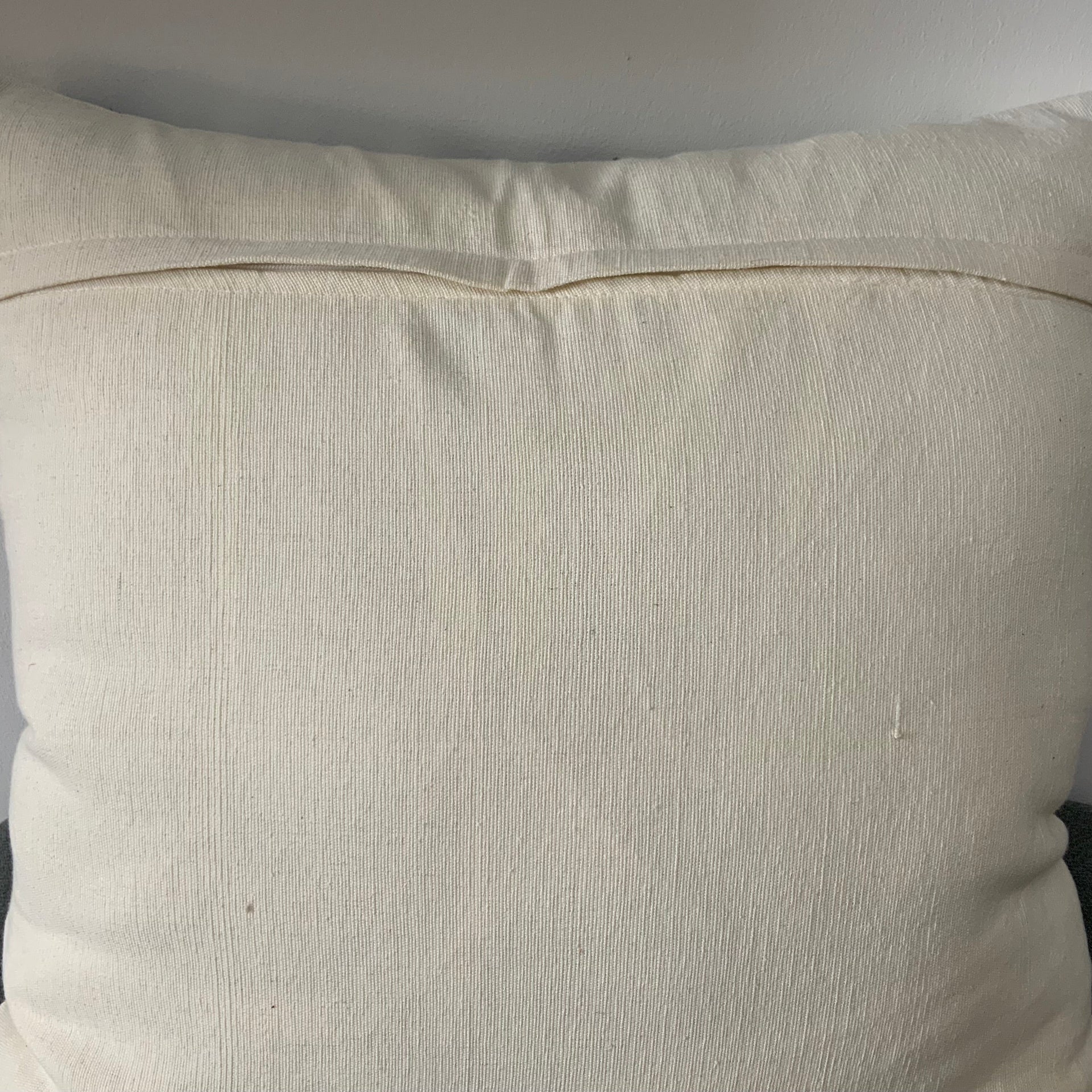 Square cream-colored throw pillow cover featuring raised black geometric embroidery in a tribal mudcloth pattern with chevrons, stripes, and dots.