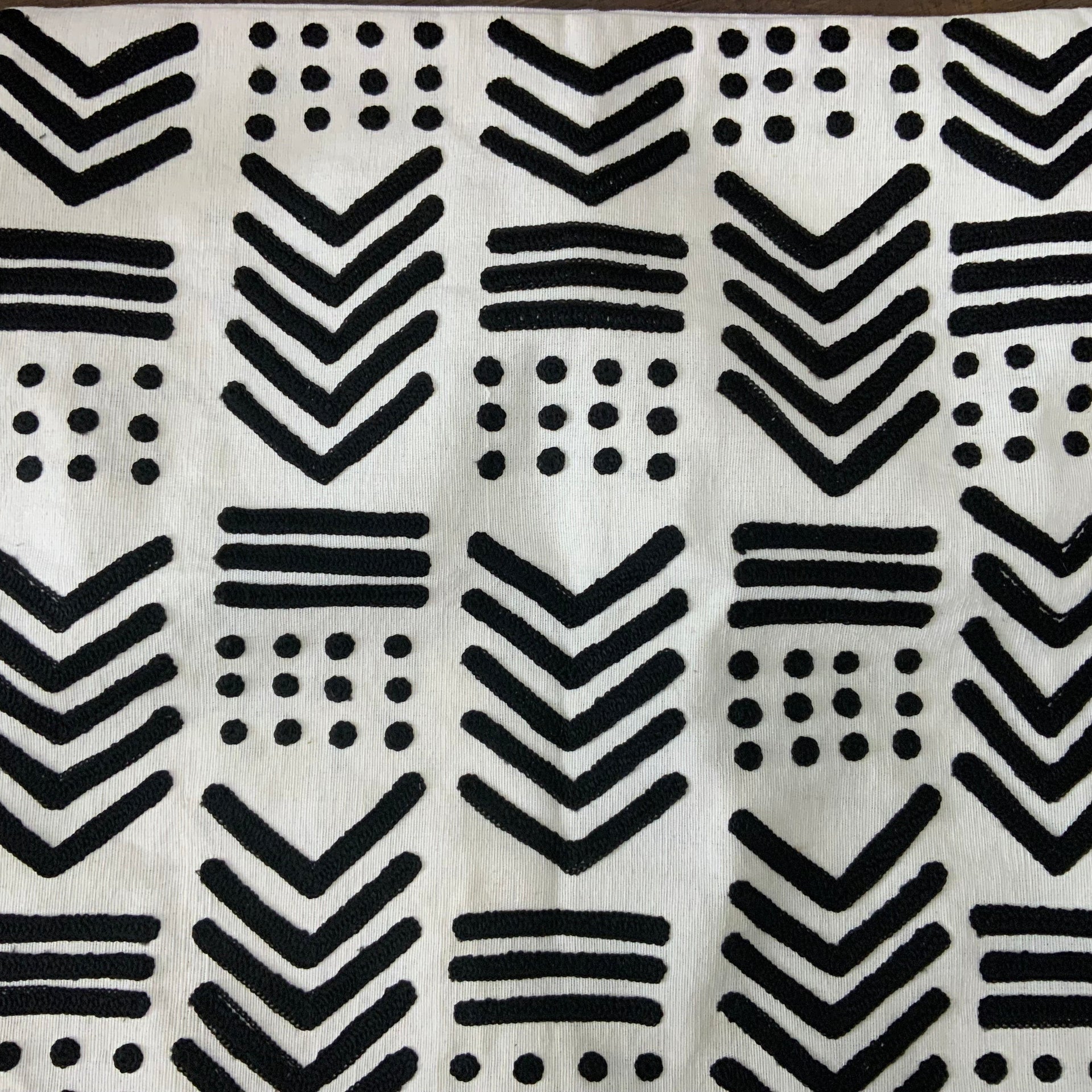 Square cream-colored throw pillow cover featuring raised black geometric embroidery in a tribal mudcloth pattern with chevrons, stripes, and dots. Square cream-colored throw pillow cover featuring raised black geometric embroidery in a tribal mudcloth pattern with chevrons, stripes, and dots.