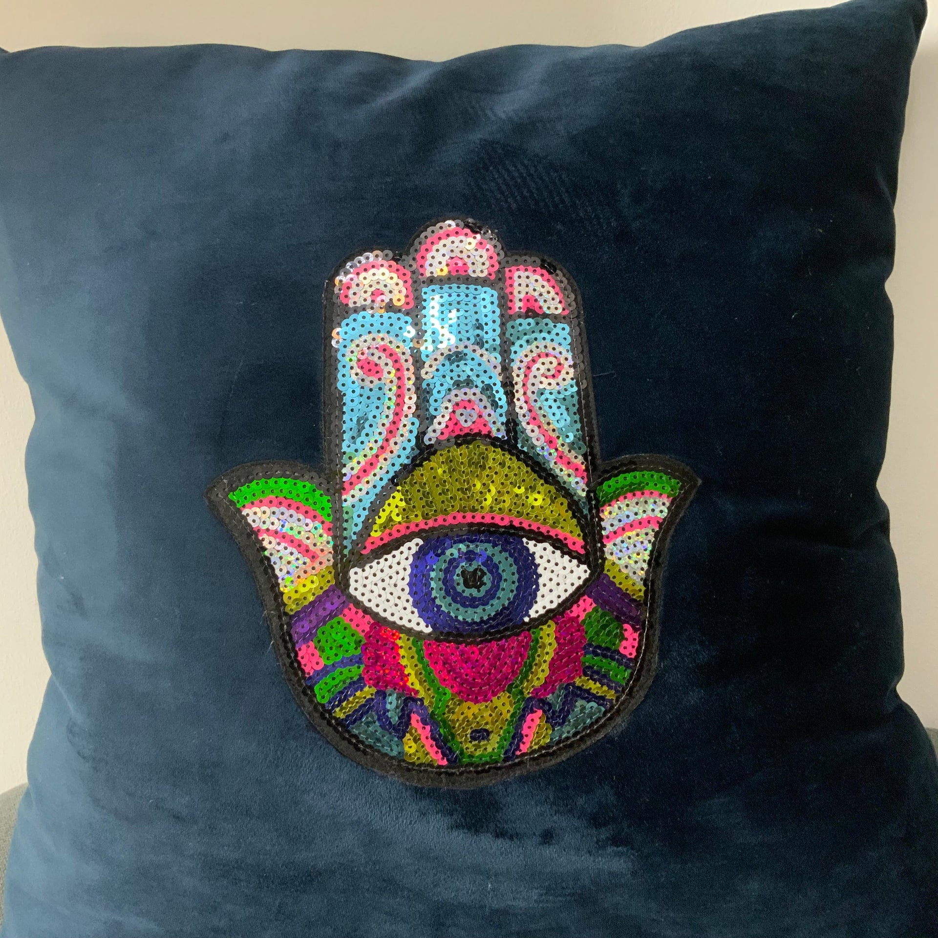Midnight blue velvet cushion cover featuring a vibrant multi-colored sequin Hamsa Hand with an evil eye symbol in the center.