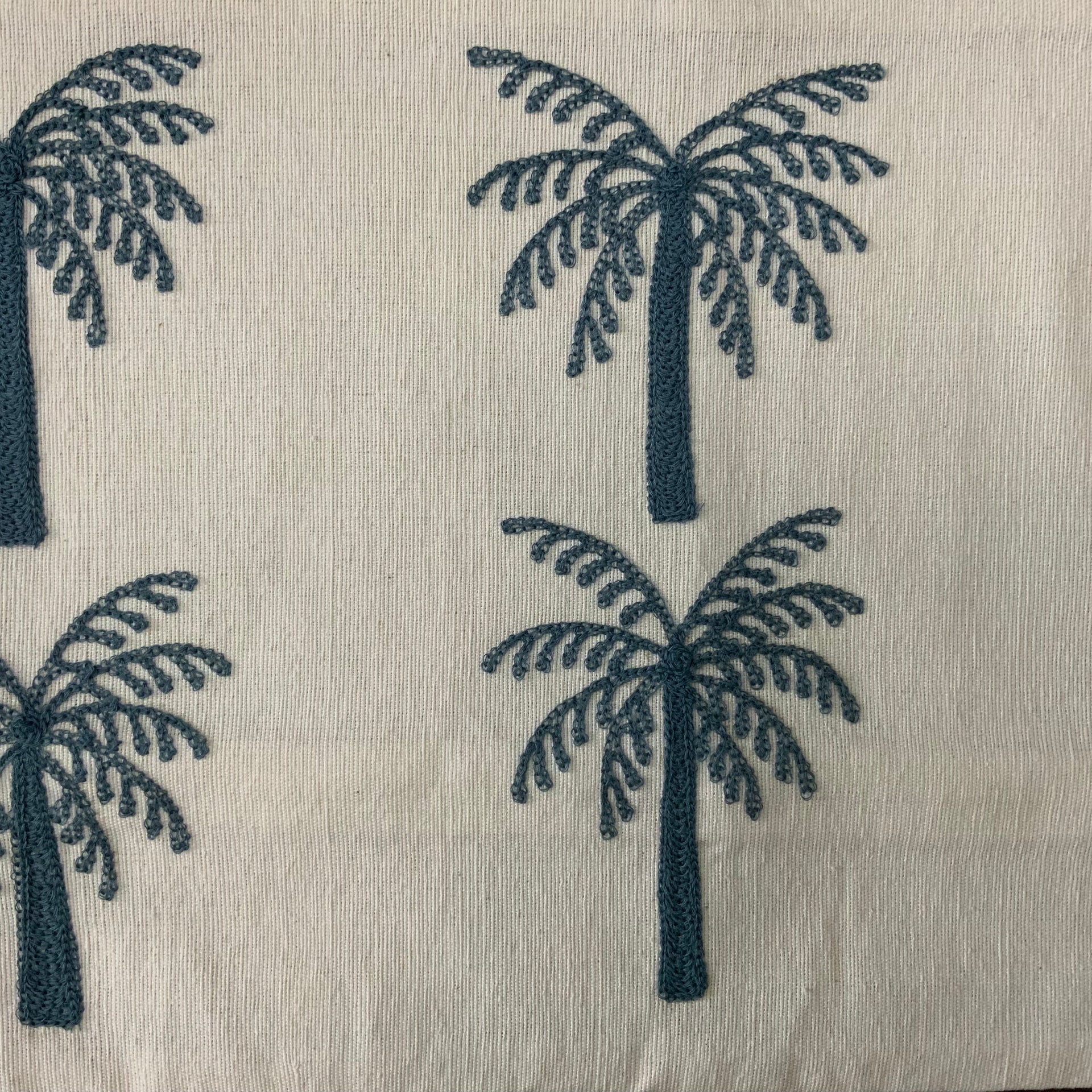 A rectangular off-white lumbar cushion featuring two rows of three identical palm trees embroidered in deep teal blue thread.