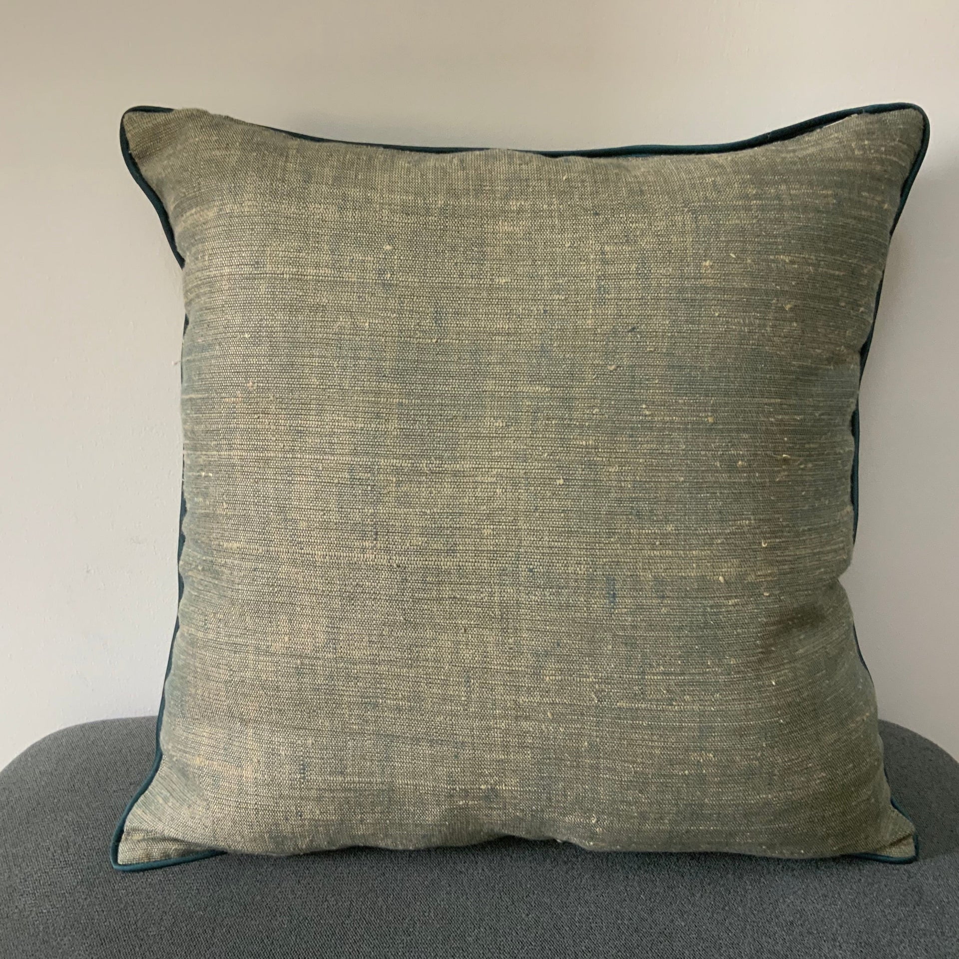 Square sage green cushion cover with a heavy slub texture and dark teal piped edges, organic woven fabric for minimalist home decor.