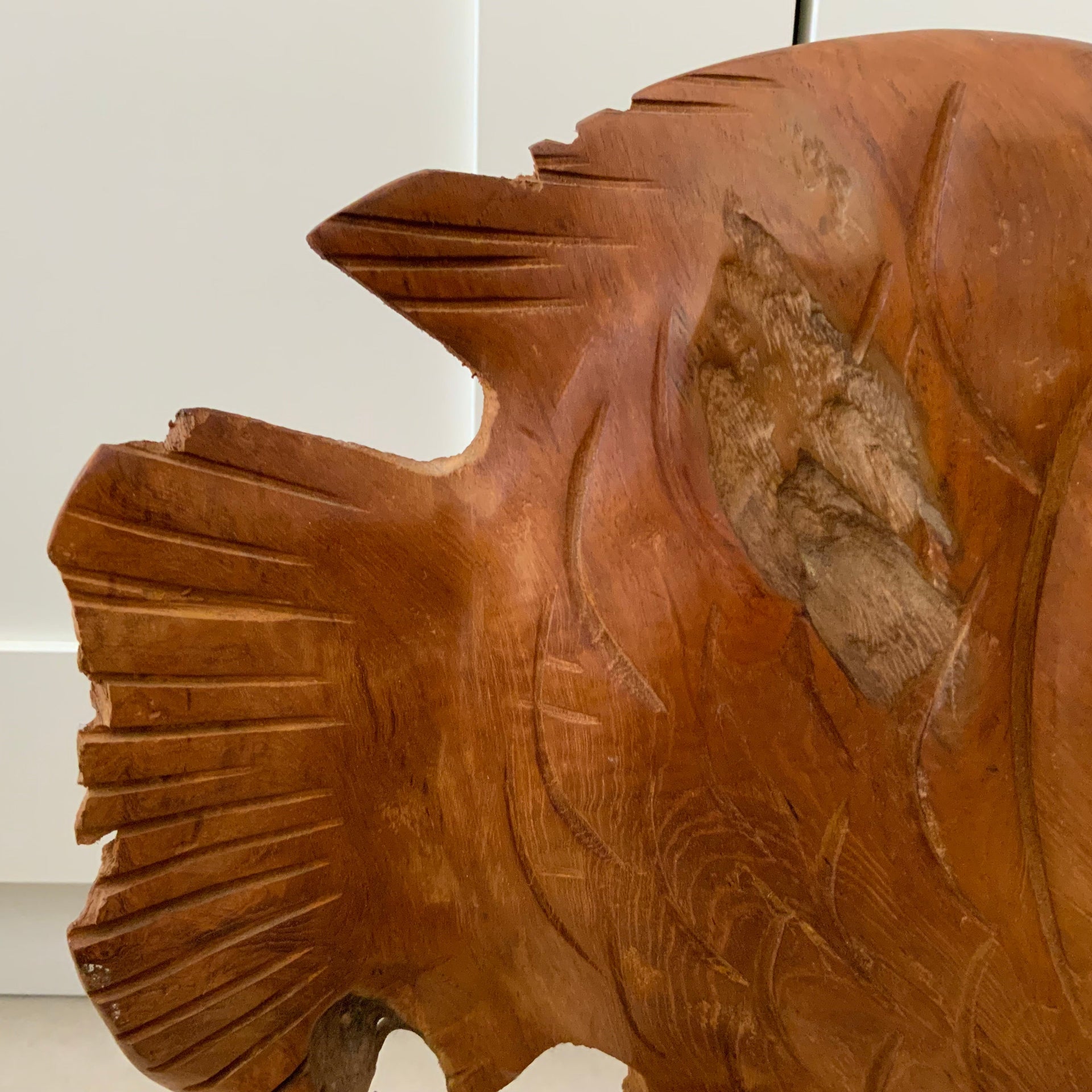 Macro view of the tail fin and rear section of a hand-carved wooden fish, highlighting the layered artisan cuts and raw wood texture.